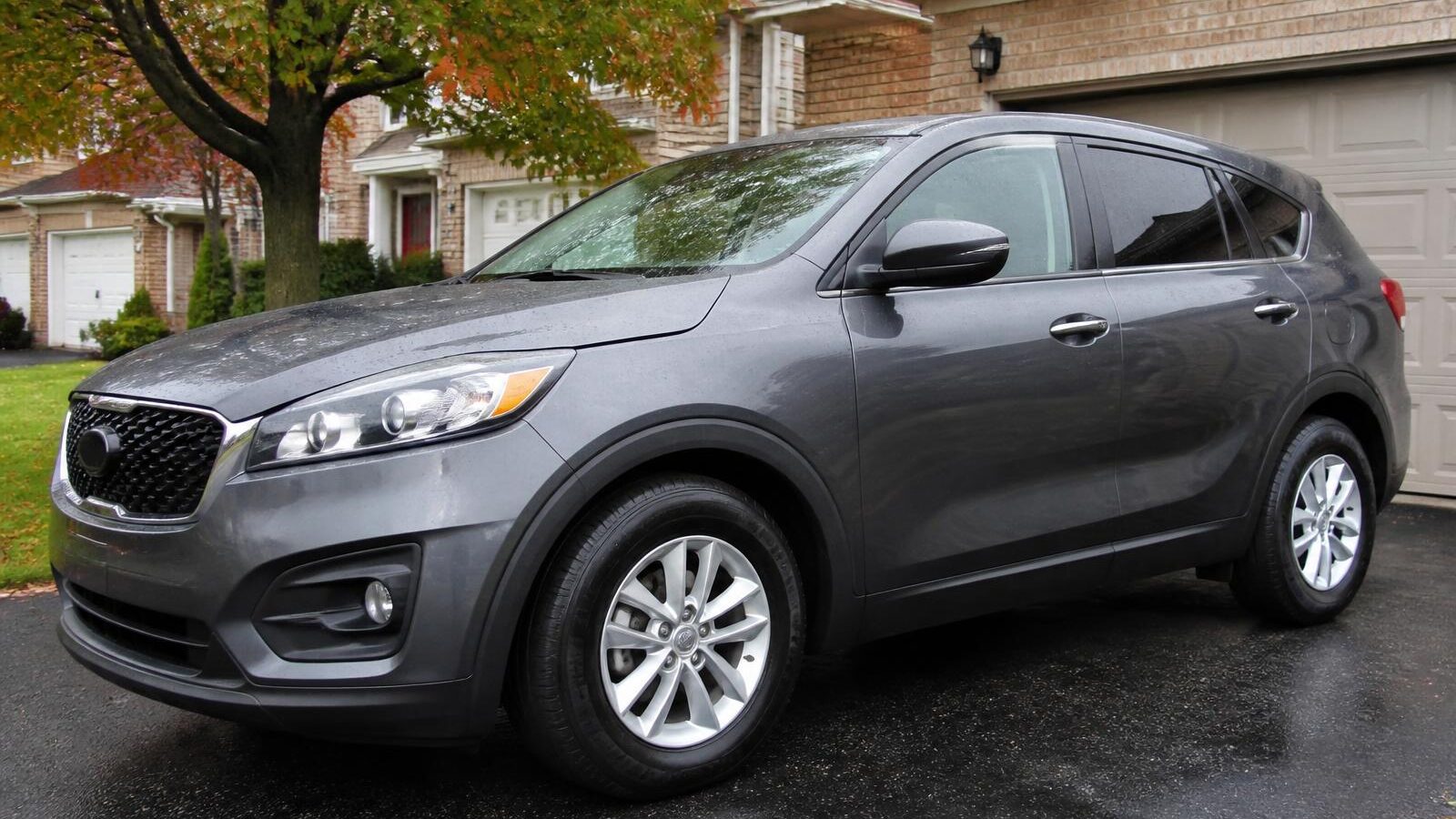 A clean grey crossover SUV parked in a residential driveway after a hand wash, water beading on the paint.